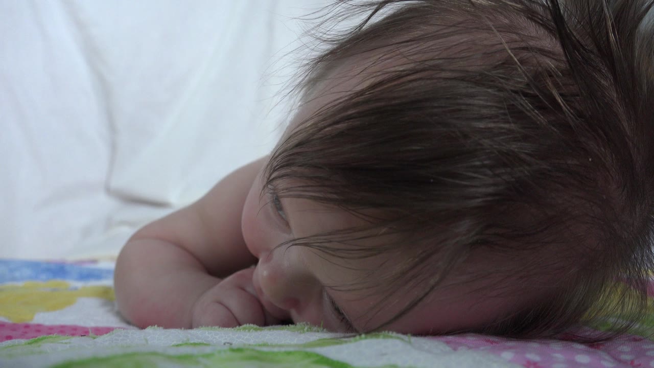 At 0:01 in Westminster, Colorado footage, the baby remains face down with one arm tucked near the cheek and dark hair spread across the head.