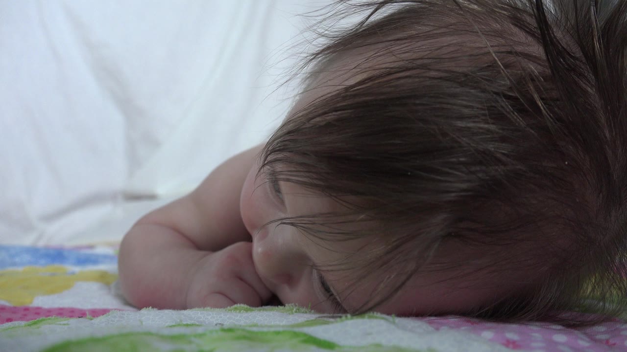 A close side view shows the infant's dark hair covering part of the face while the cheek rests near the patterned blanket in Westminster, Colorado.