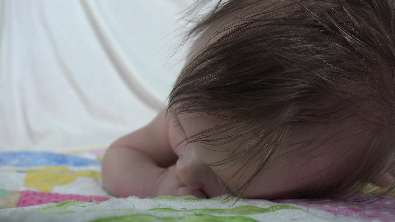 Infant lying face-down on a colorful quilt indoors.