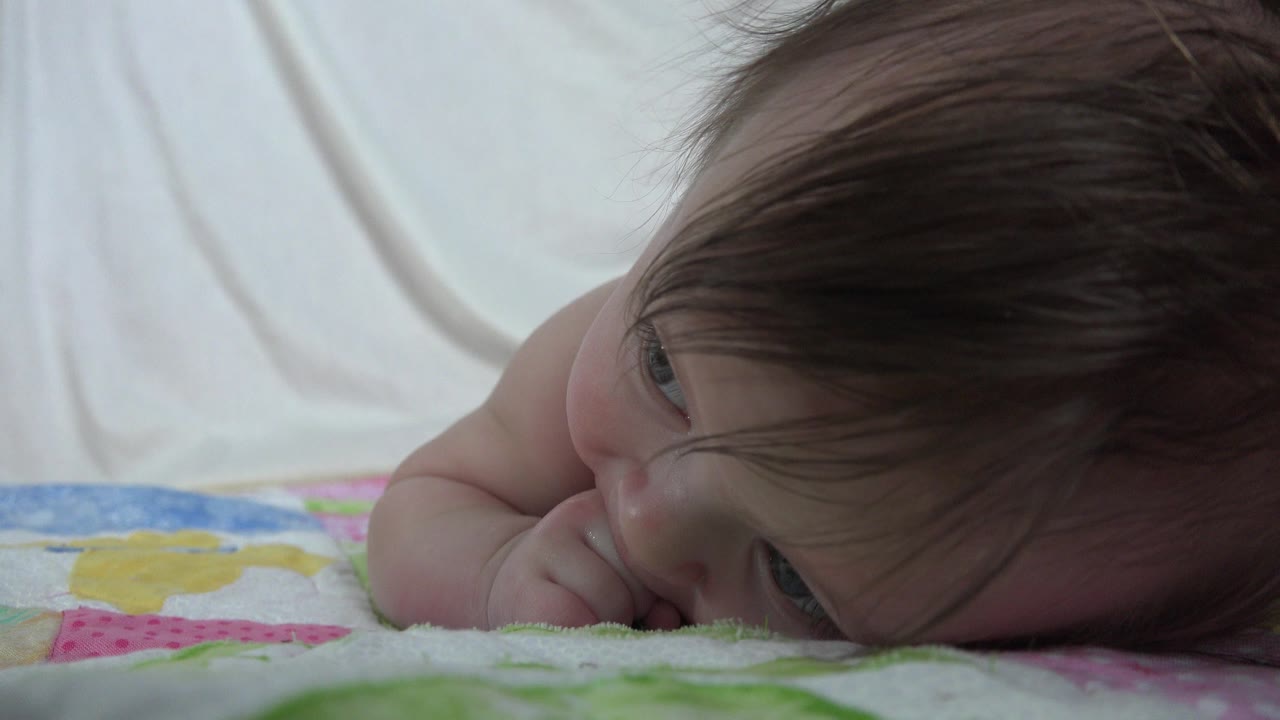 Baby lying sideways on a patterned blanket.