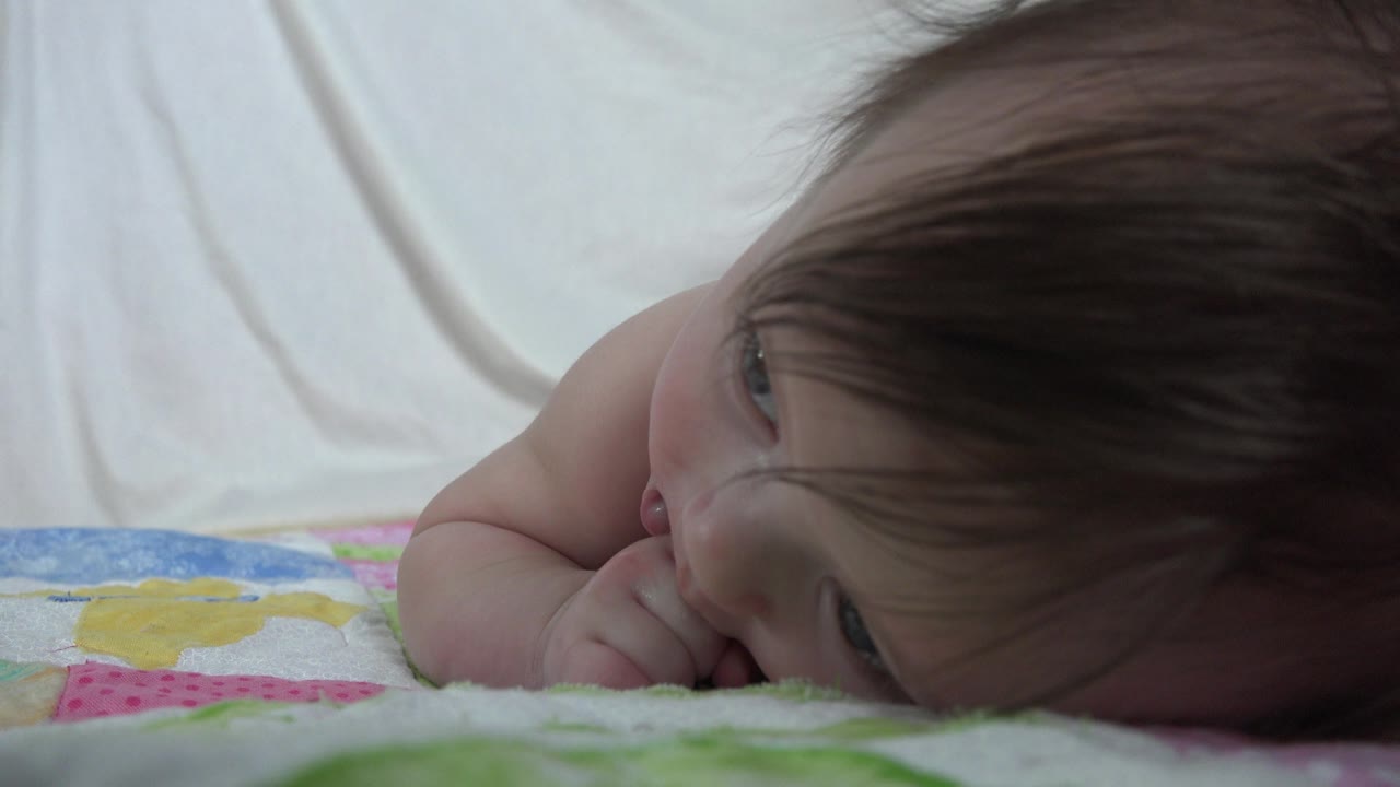 A close bed-level frame in Westminster, Colorado, shows the baby lying near the edge of the patterned blanket with the face partly obscured by hair.