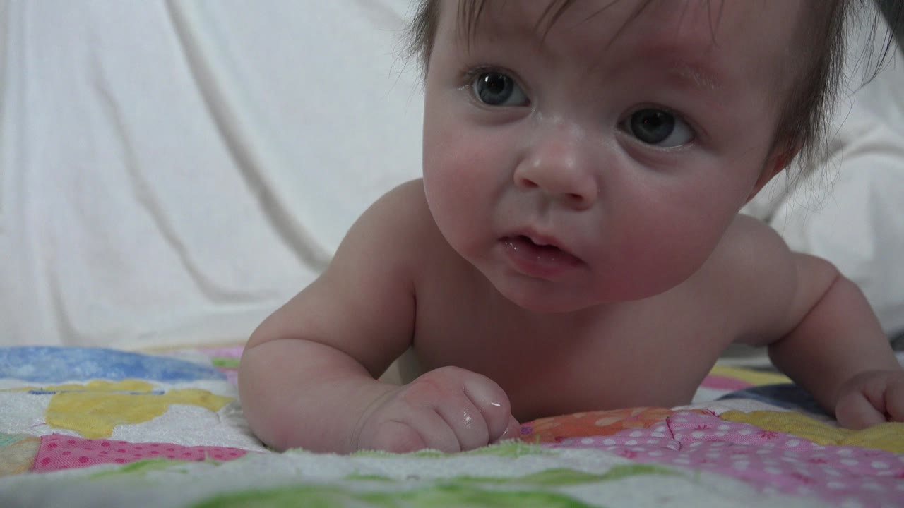 Baby lying on stomach on a colorful blanket.