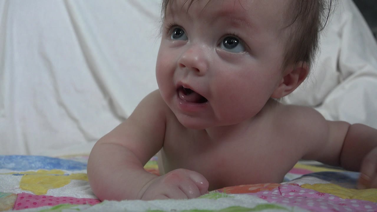 Baby lying on a colorful blanket and looking upward.
