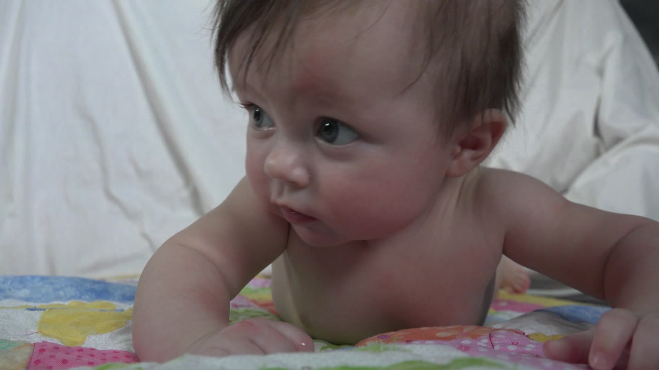 Baby lying on a colorful blanket and looking left.