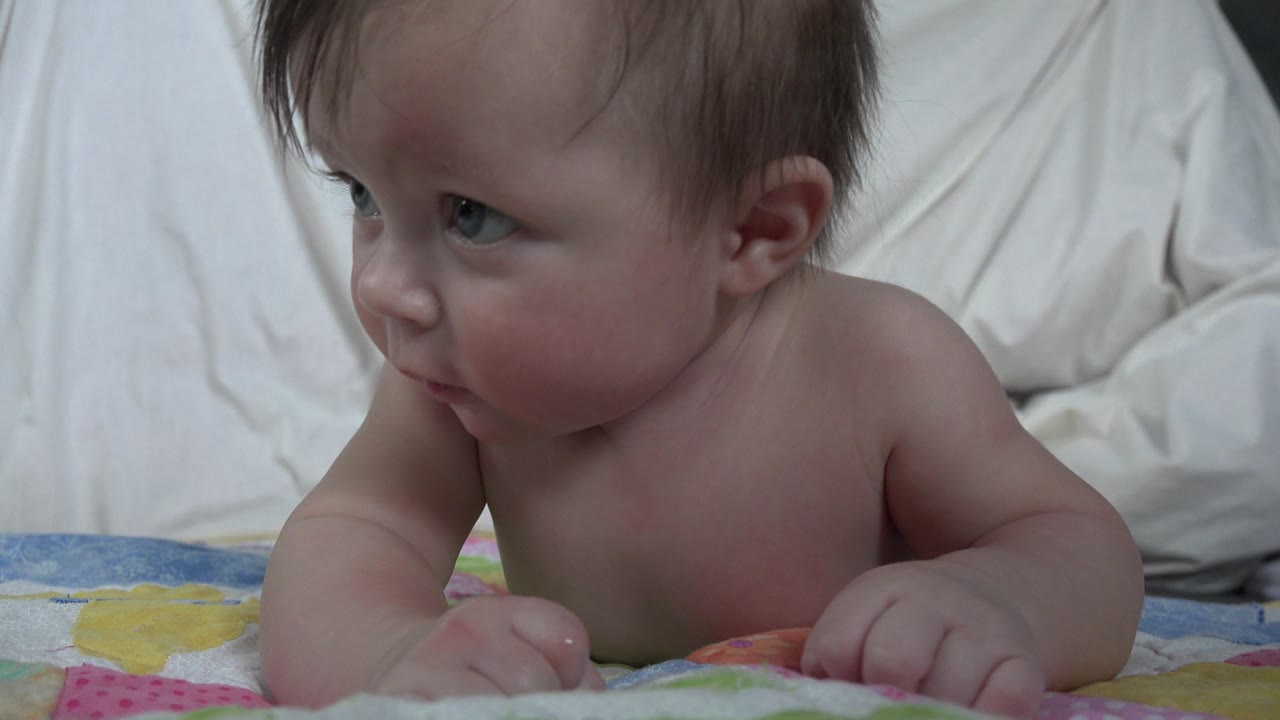 Baby lying on stomach and looking toward the left side of frame.