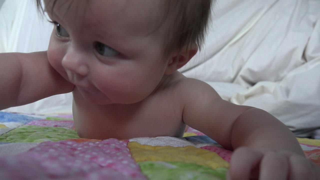 Baby lying on a colorful blanket and looking left.