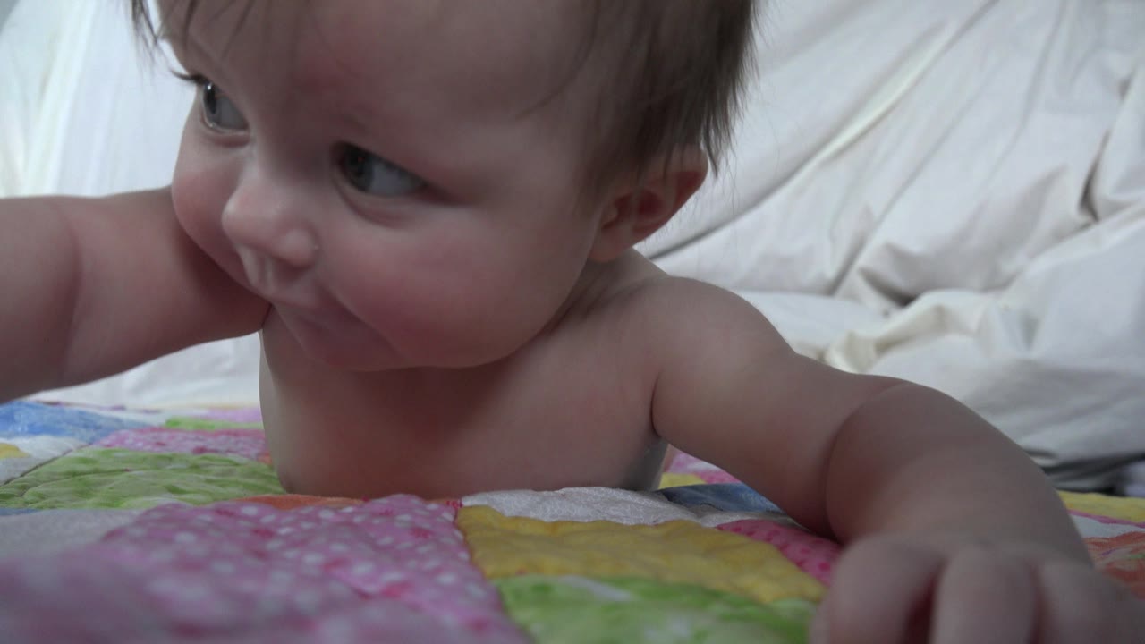 The baby remains low on the colorful blanket in Westminster, Colorado, with one arm forward and the face turned toward the left side of frame.