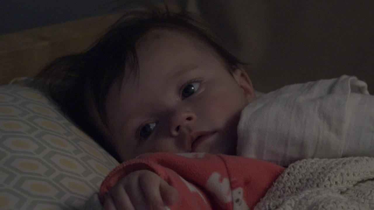 Baby resting with eyes open beside a white blanket.