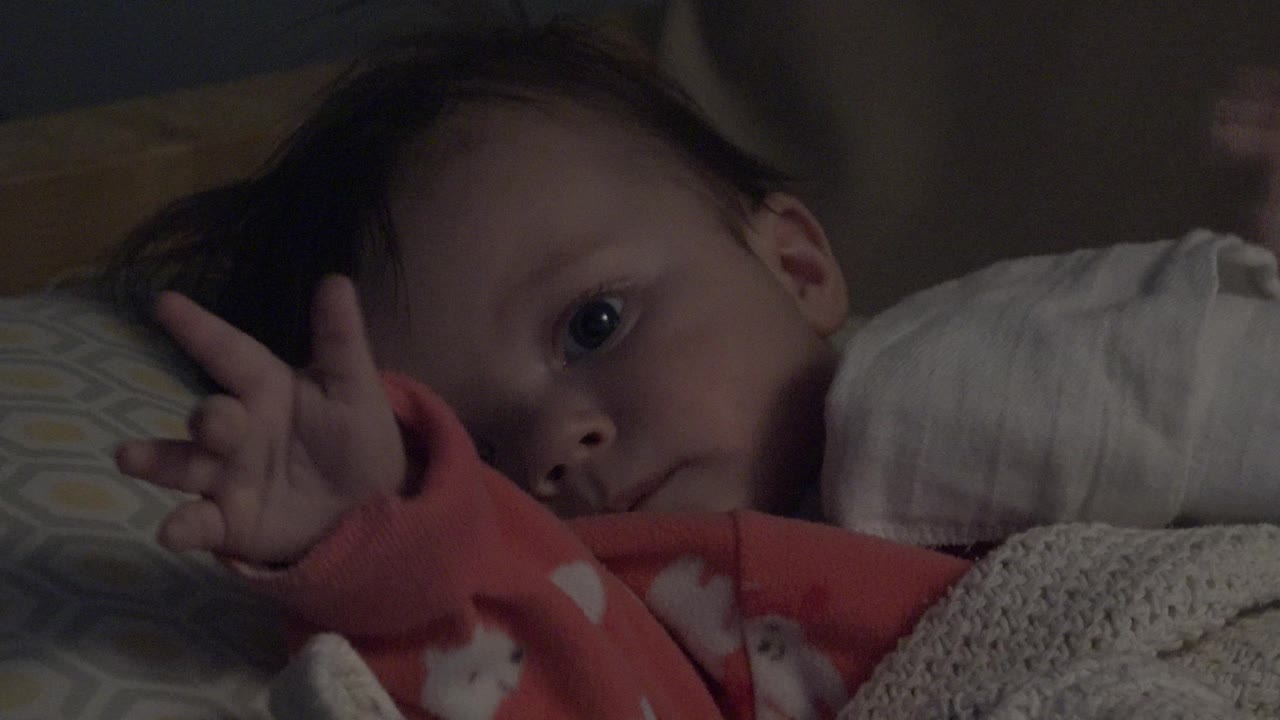 Baby looking toward the camera with a hand open beside the head.