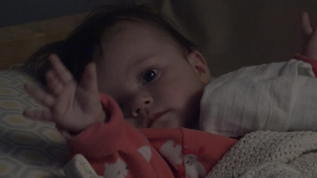 In Westminster, Colorado, the baby remains tucked among pillows as a hand lifts near the forehead and the face stays turned toward the camera.