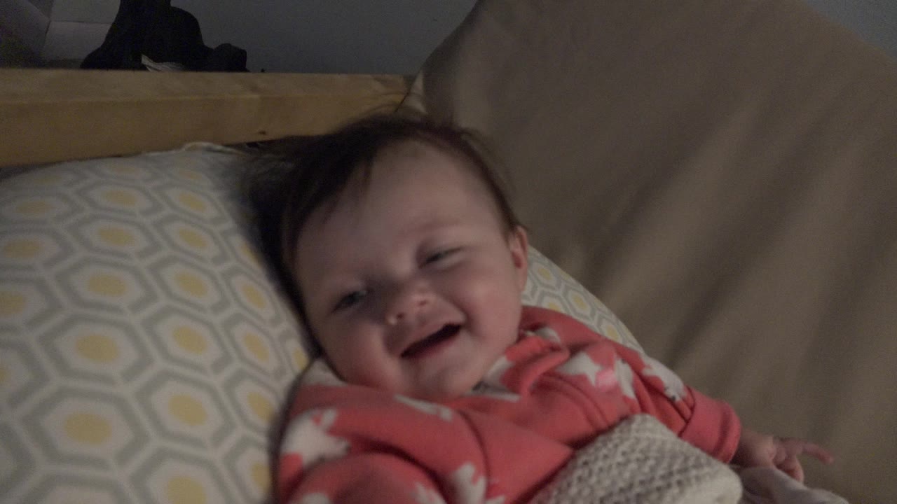 Baby smiling while lying beside a patterned pillow.