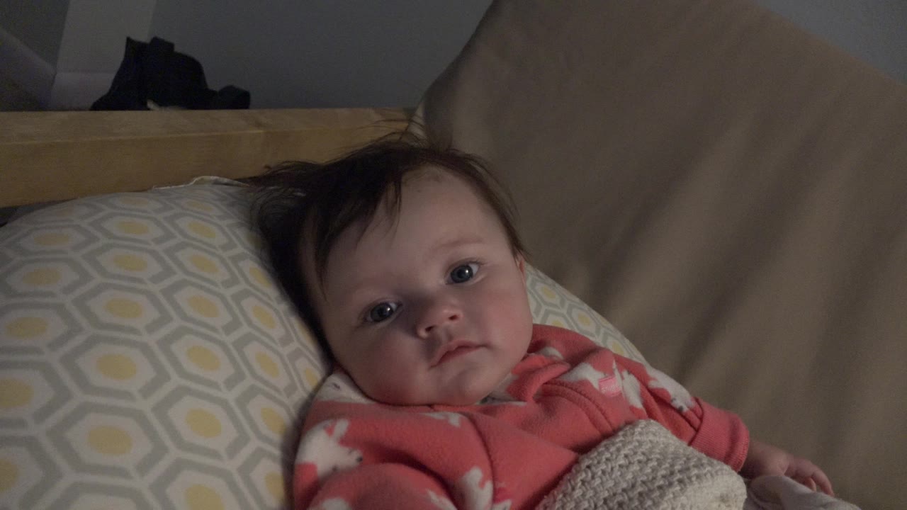 Baby girl lying on a patterned pillow under a blanket on a couch.