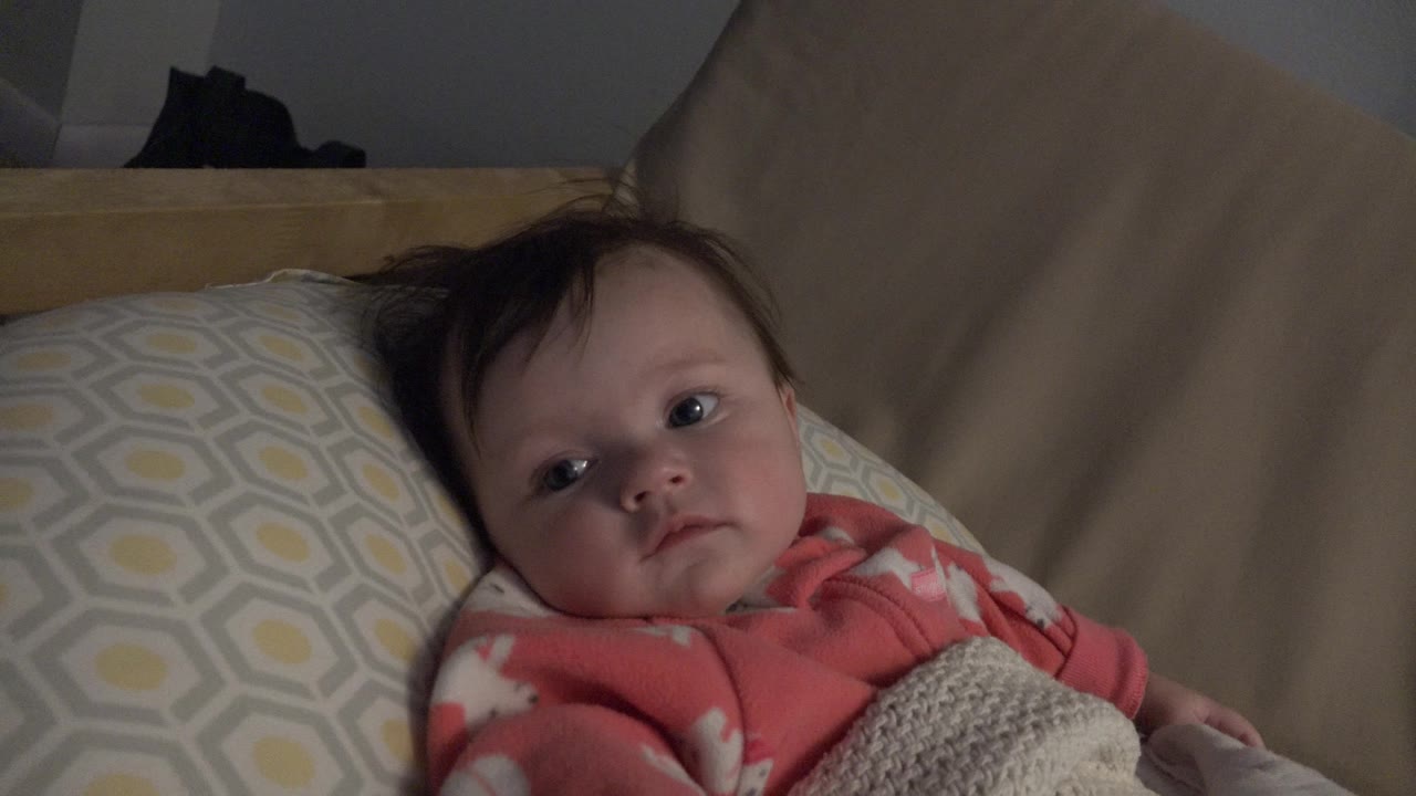 Baby lying on a patterned pillow under a light blanket.