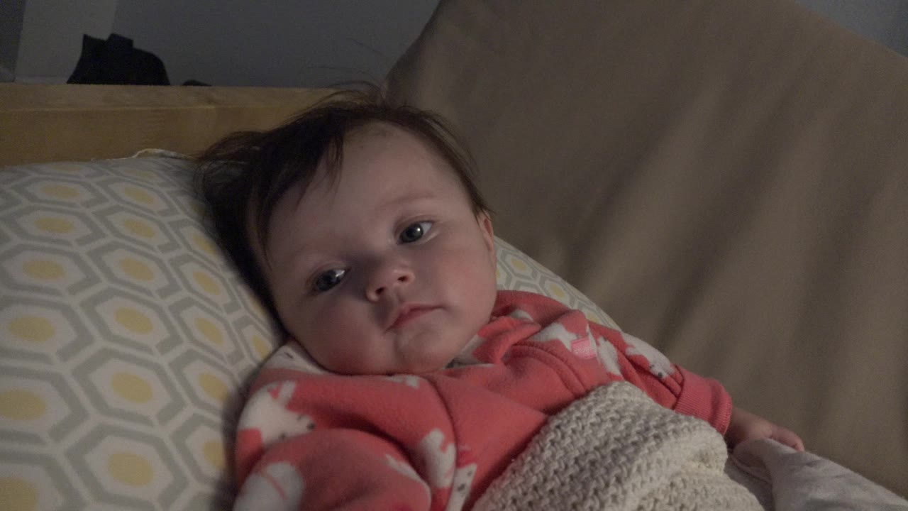 Baby lying in a crib under a knitted blanket.