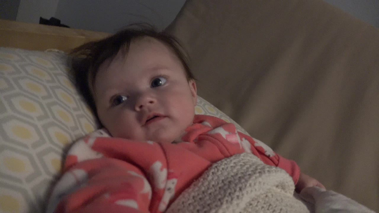 Baby lying on a bed under a knitted blanket.