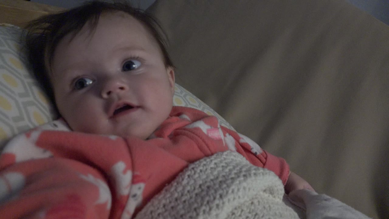 Baby lying in bed under a knit blanket
