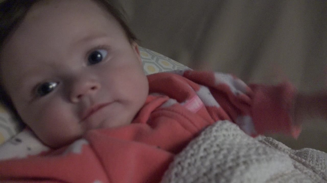 Baby in pink pajamas lying in a crib under a blanket.