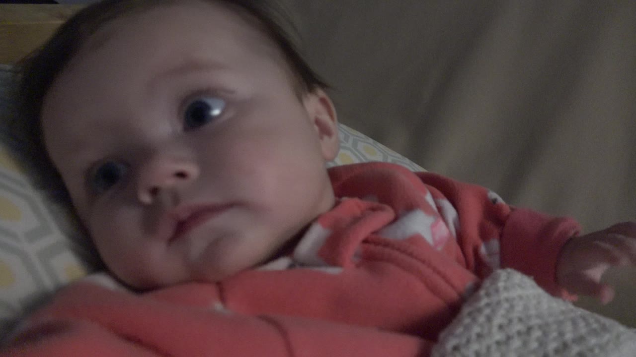 Baby lying on bedding in a coral sleeper.