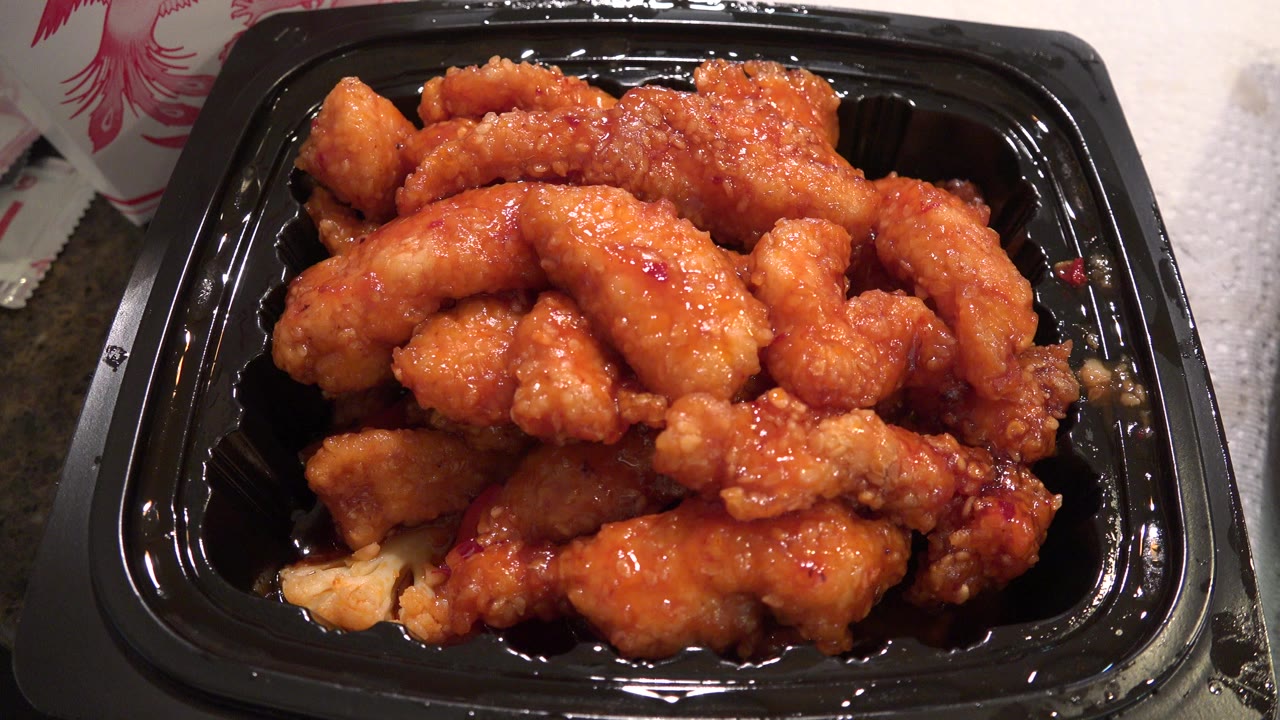 Sauced fried chicken in a black plastic tray on a countertop.