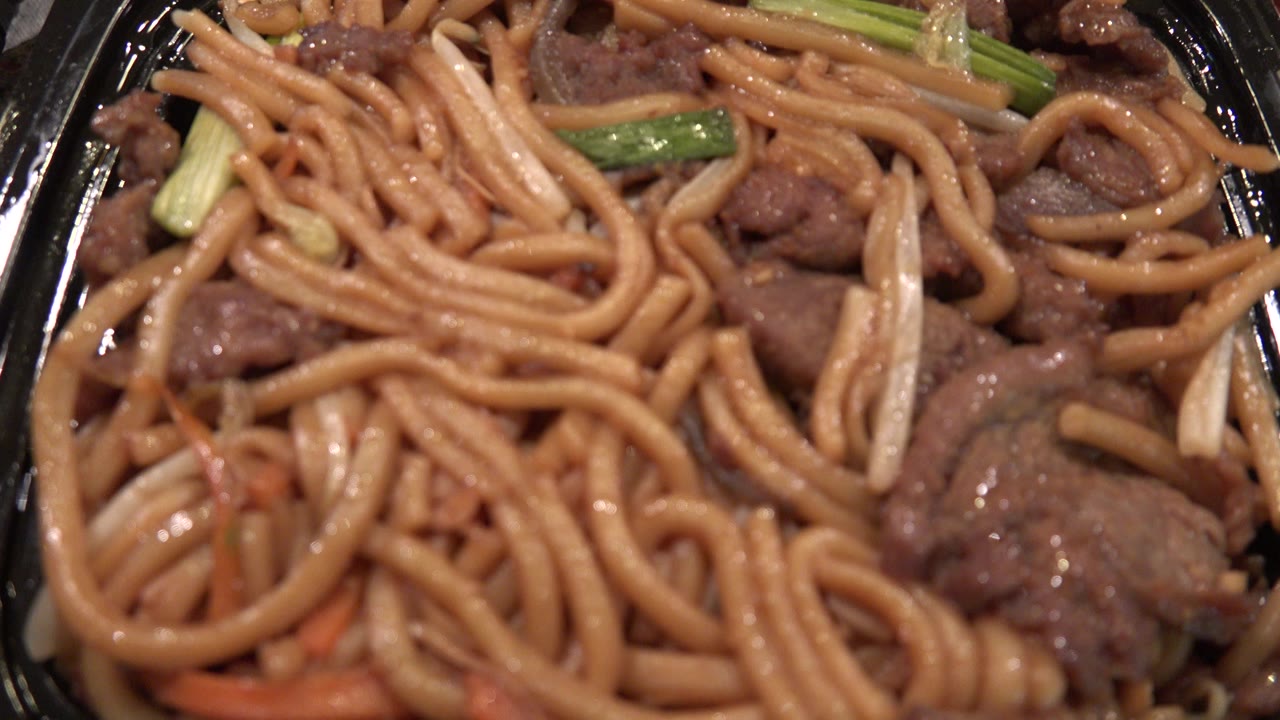 Close-up of sauced noodles and meat in a black takeout tray.