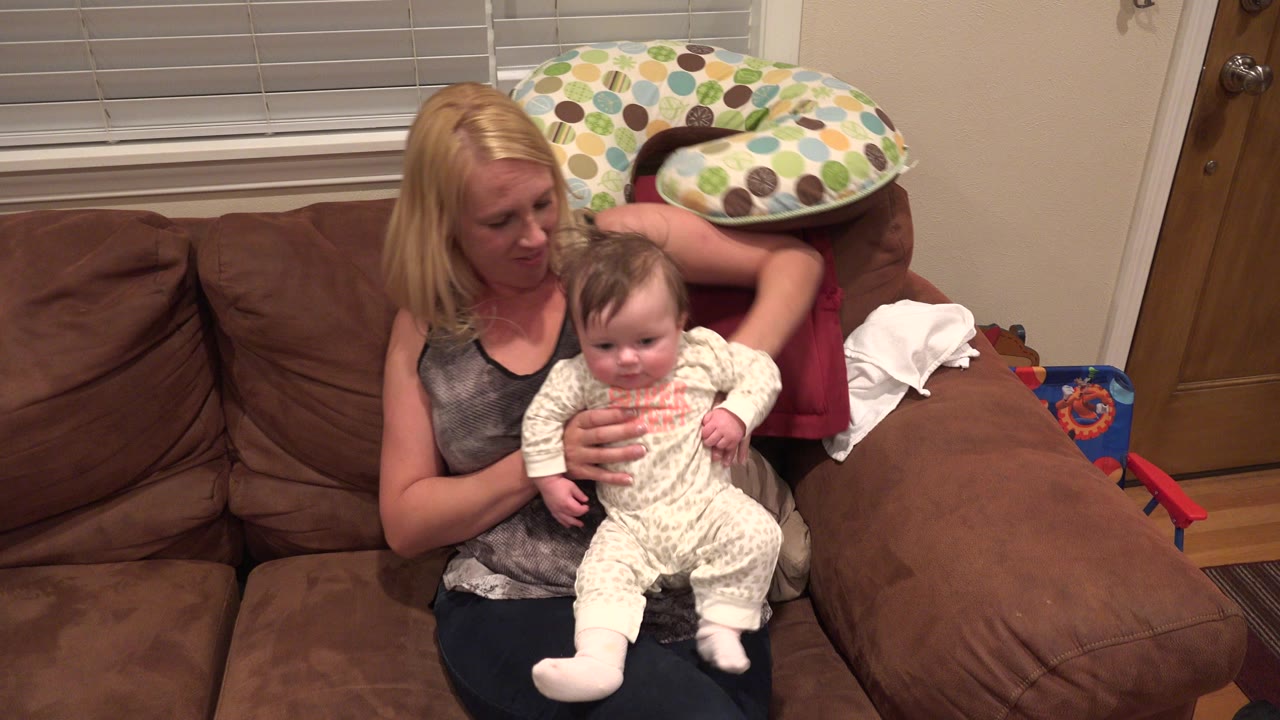 Mother sitting on a brown couch while holding a baby.