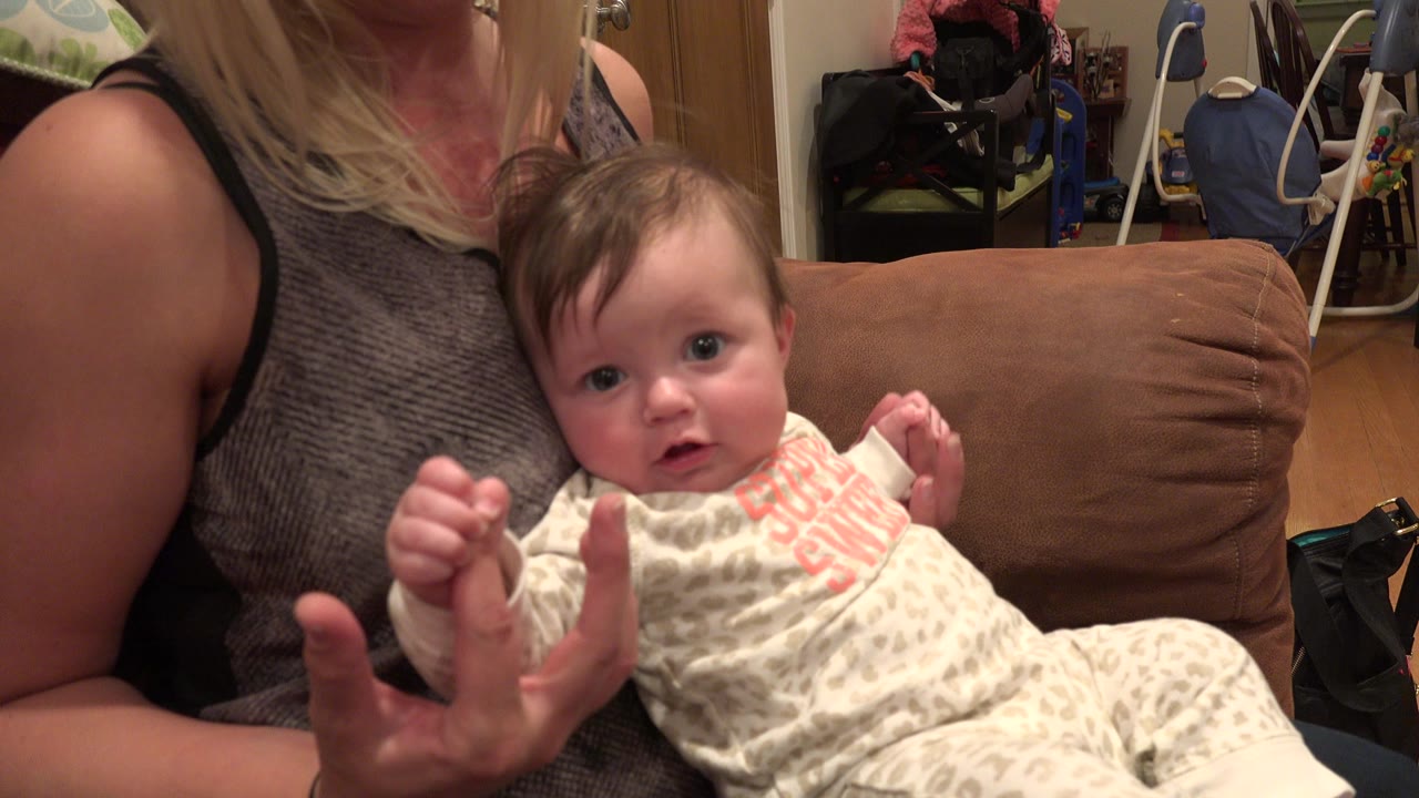 Mother holding a baby on a brown couch indoors.