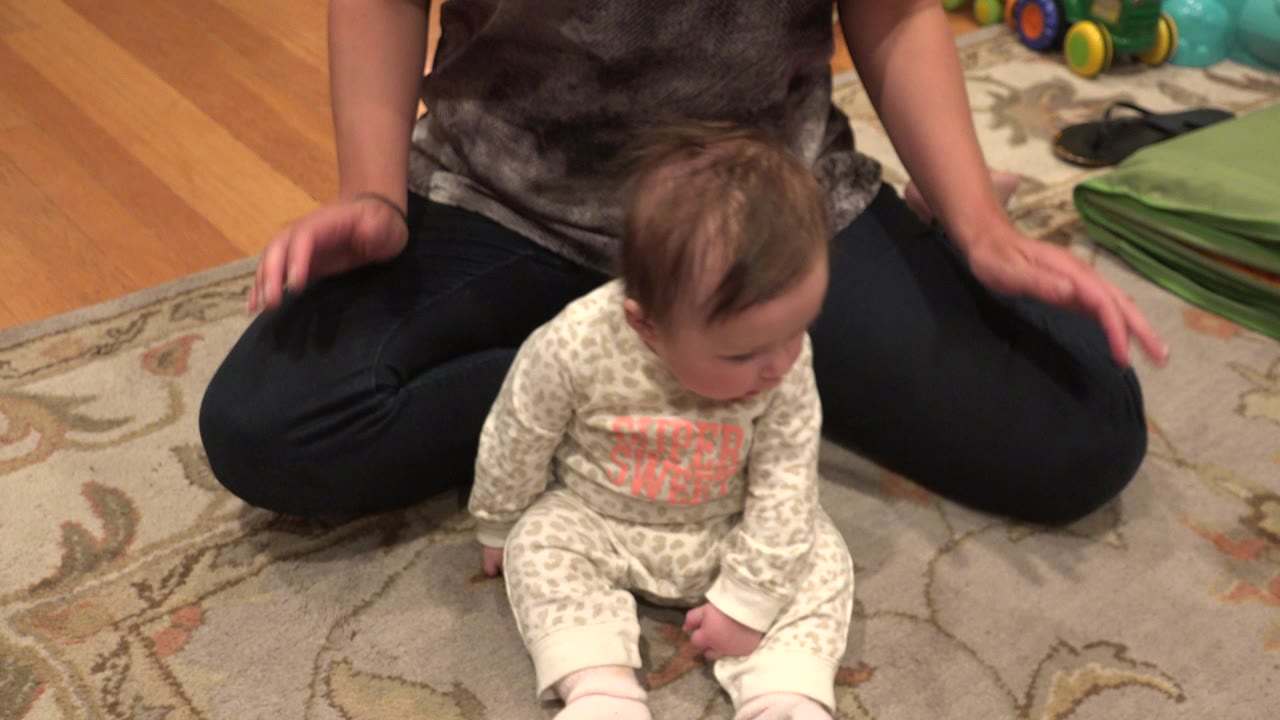 Baby sitting on a rug between an adult's legs.