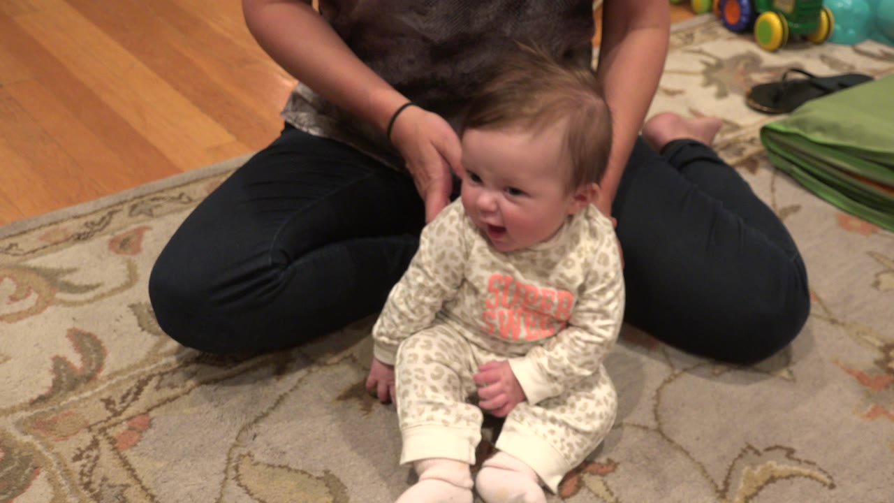 In Westminster, Colorado, the baby turns slightly to one side on the rug as the adult's hands remain near the child's head and shoulder.