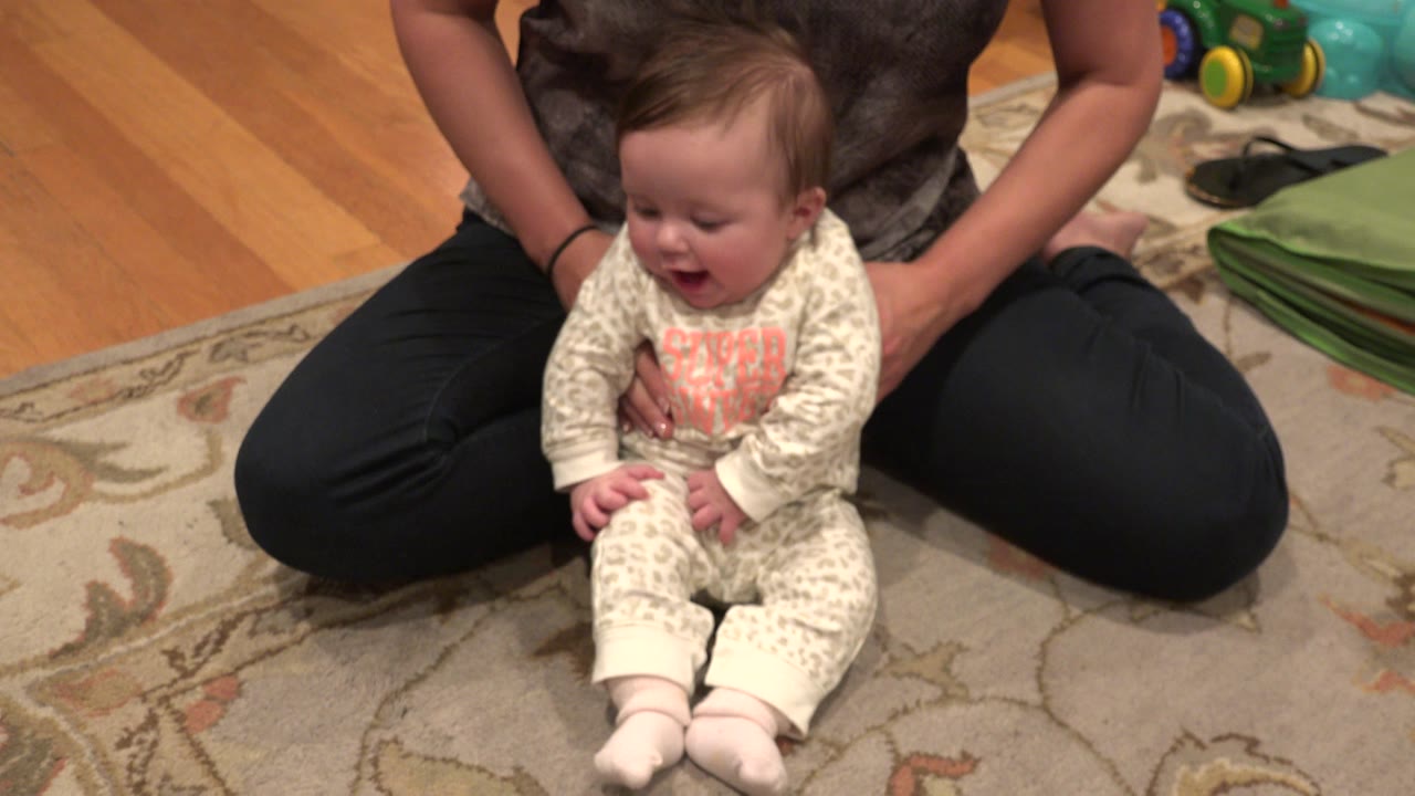 Baby sitting on a carpet with mother behind them.
