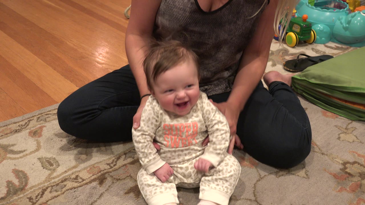 At 0:00 in Westminster, Colorado, a smiling baby sits on a patterned rug while an adult woman seated behind supports the child in a home interior.