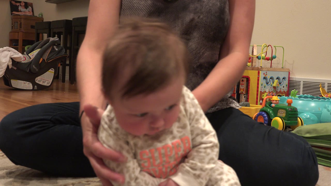 In Westminster, Colorado, the baby remains bent forward near the camera as the seated adult steadies the child's torso from behind.