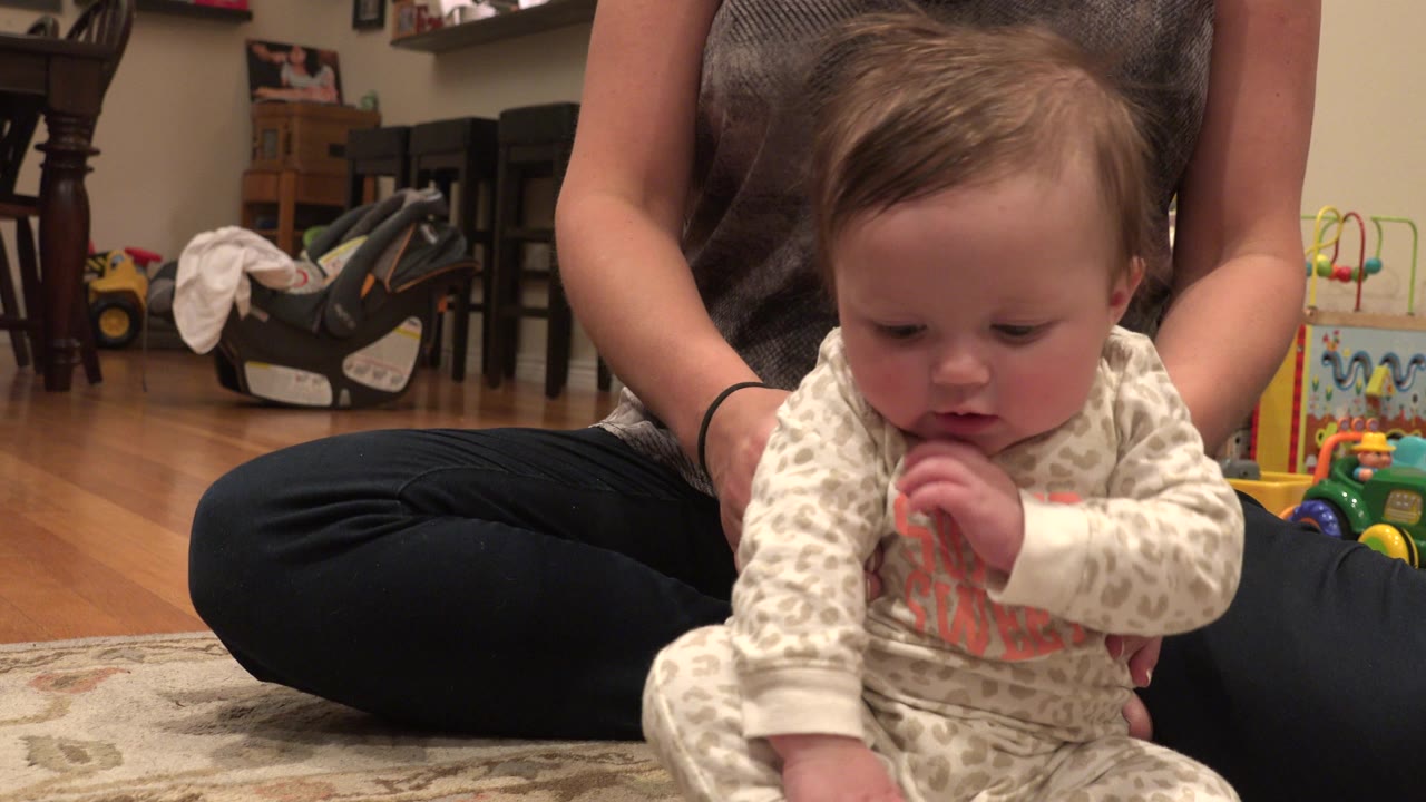 In Westminster, Colorado, the baby looks down with fingers near the mouth while the woman seated behind keeps both hands around the child's sides.