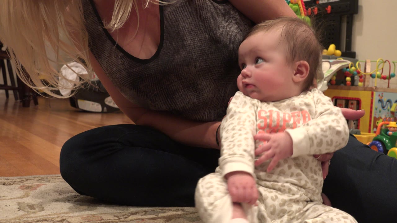 In Westminster, Colorado, the baby remains seated in the foreground, looking left while the adult's hands and torso stay close behind for support.