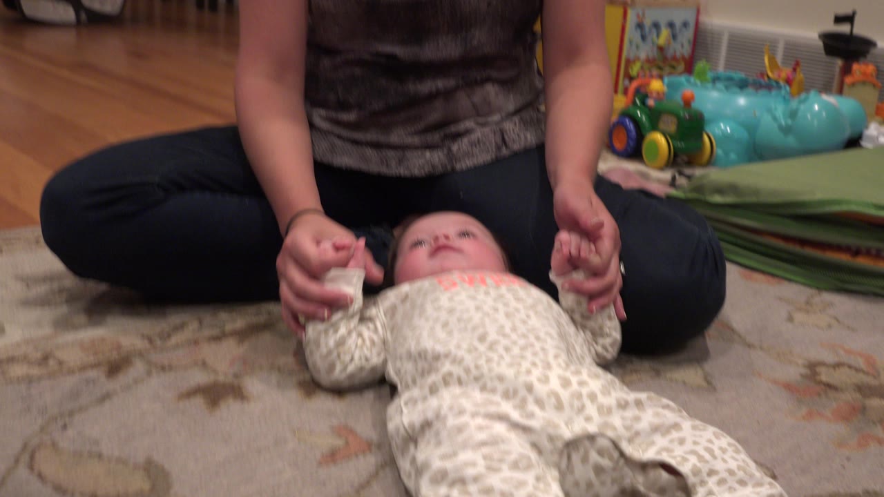 Adult holding a baby's hands as the baby lies on a rug.