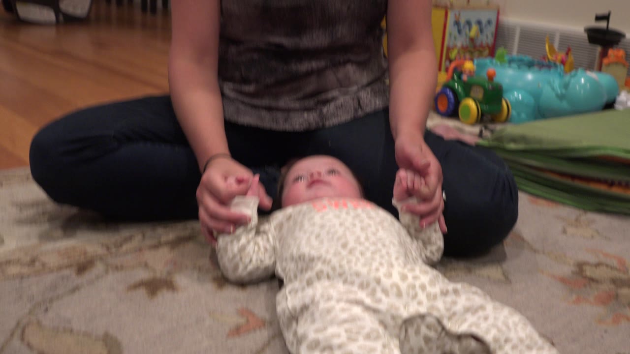 In Westminster, Colorado, the baby looks upward while the adult's hands hold both of the baby's hands over the rug.