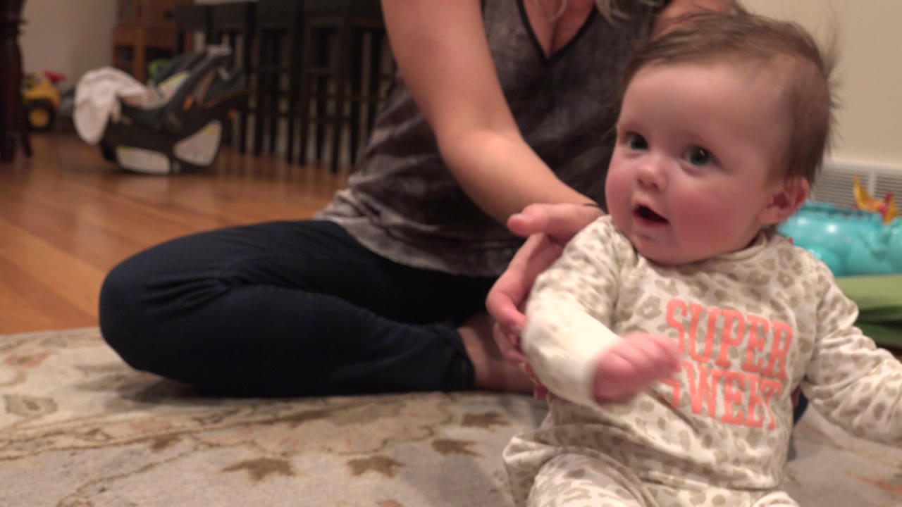In Westminster, Colorado, an infant sits upright on a patterned rug while a mother seated behind supports the baby with one hand.