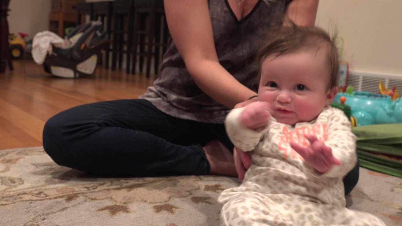 Infant raising hands while mother supports from behind.