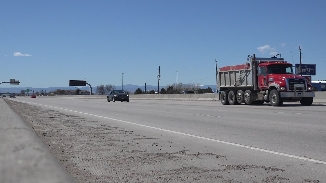 Red dump truck and dark car on a divided highway under blue sky.