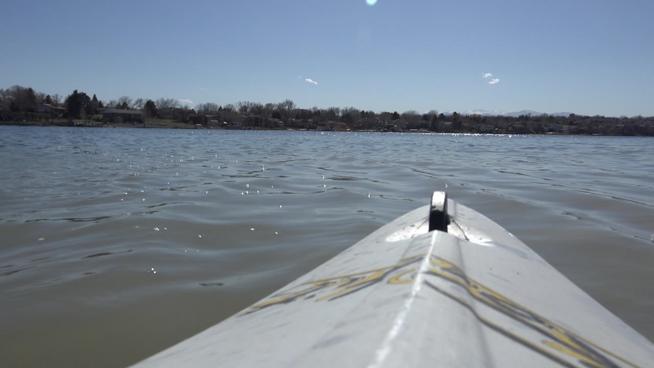 At 0:00, the white bow of a boat points across rippled water toward the tree-lined shore of Hidden Lake, Colorado, with no visible people.