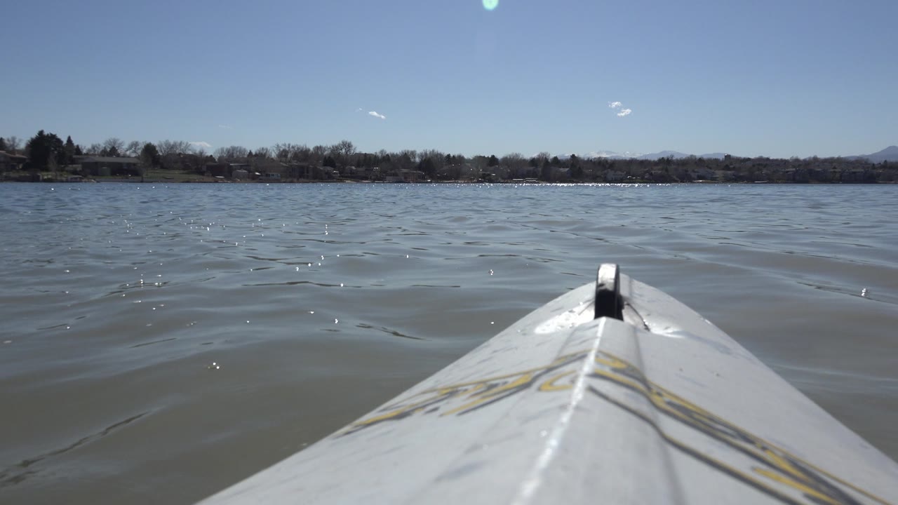 Low boat perspective over lake water with shore trees and distant mountains.