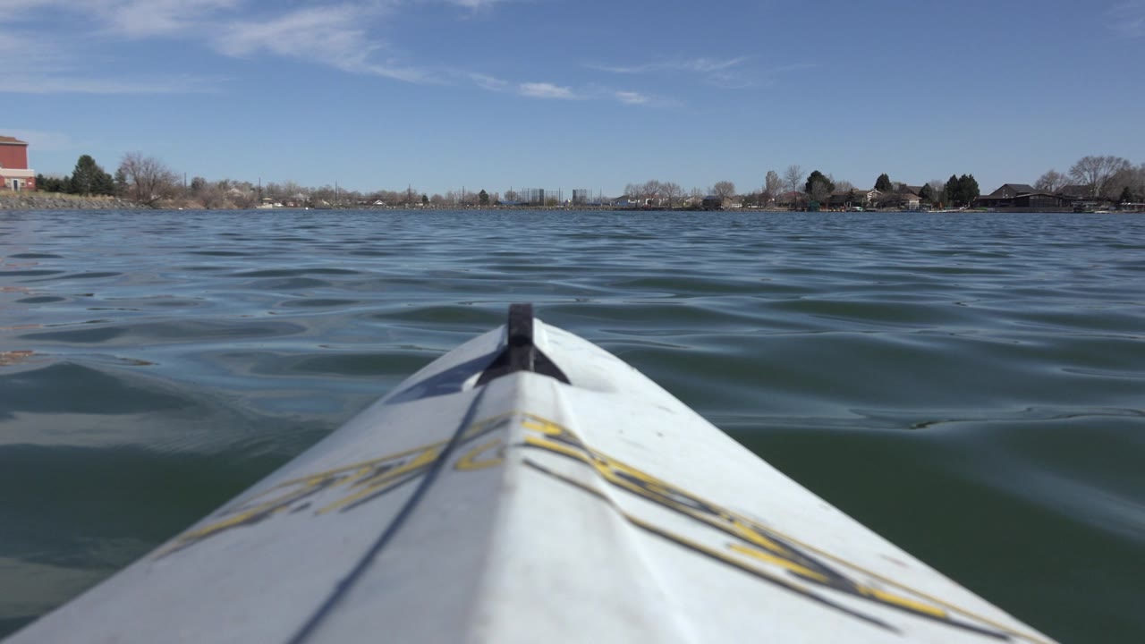 Centered kayak bow rides over small blue-green waves on Hidden Lake, Colorado, with the shoreline sitting low under a clear sky and no visible people.