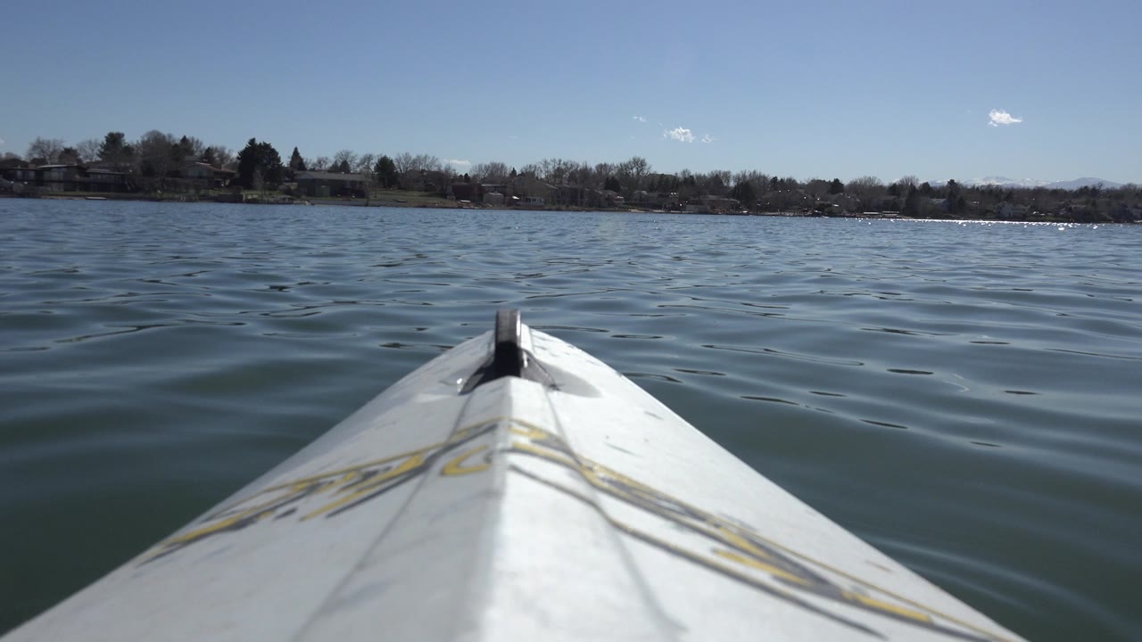 At 0:01, the white pointed bow remains centered while small waves spread across Hidden Lake, Colorado, with the shoreline low on the horizon and no visible people.