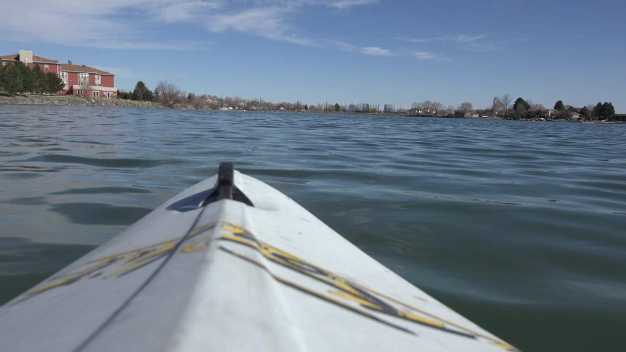 Canoe bow pointed across rippled lake water toward a distant shoreline.