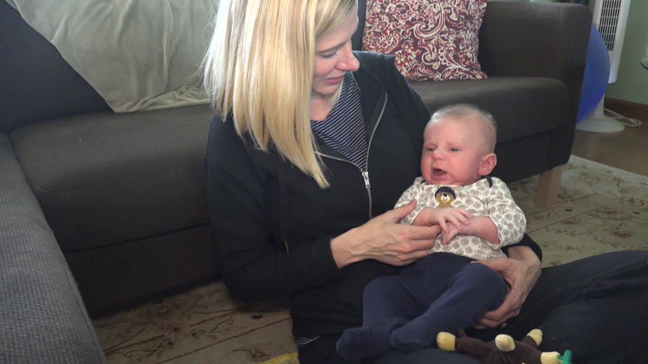 Mother holding a baby while seated on a living-room floor.