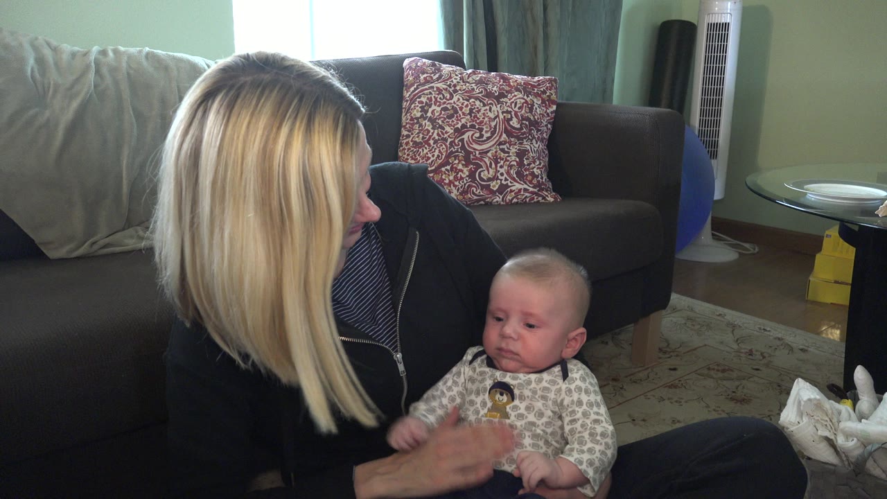 Blonde woman seated on the floor holding an infant in a living room.