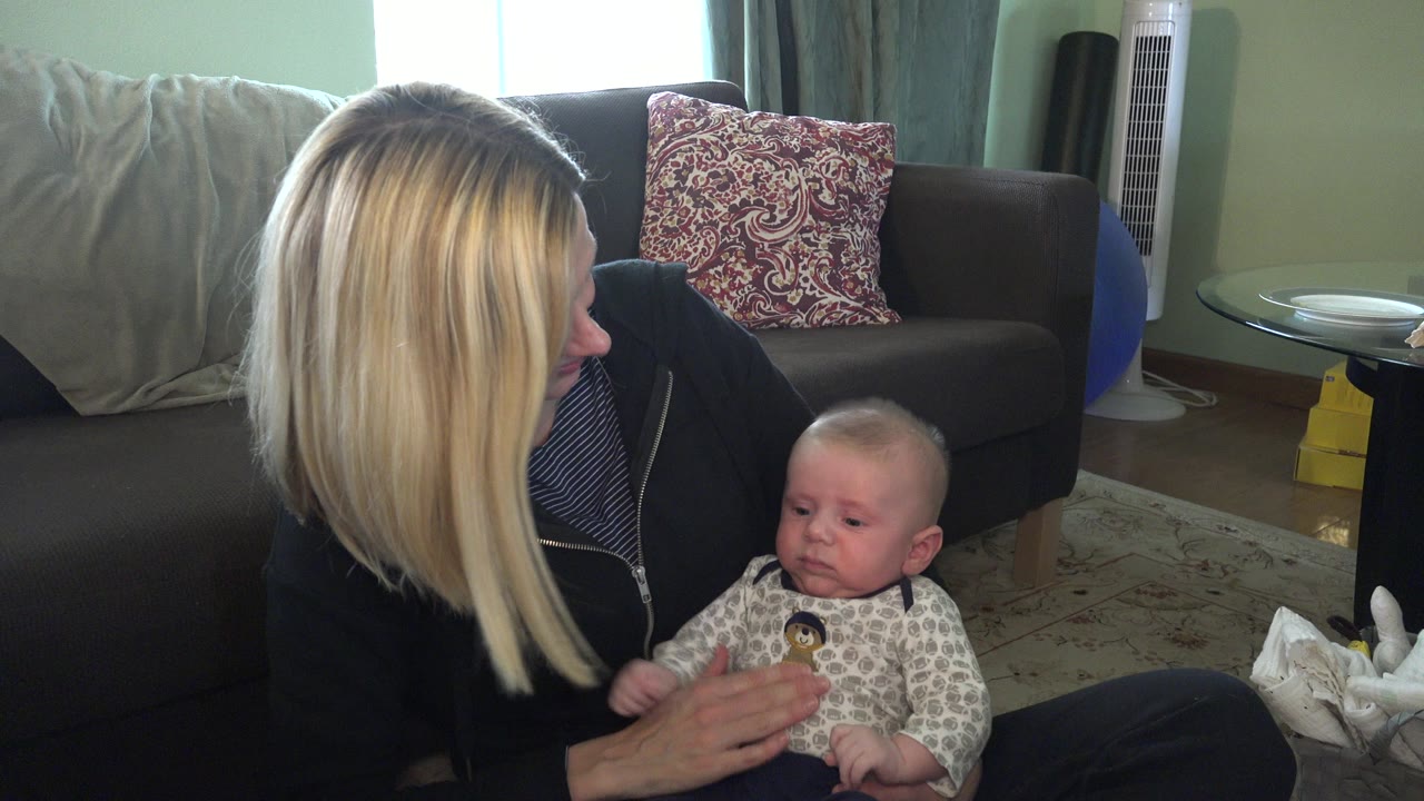 At Hidden Lake, Colorado, the woman remains seated on the floor facing the infant, with patterned pillows and a bright window behind the sofa.