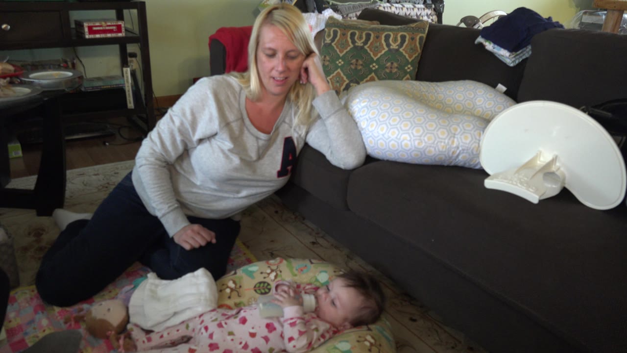 Smiling blonde woman beside a baby lying on a mat near a couch.