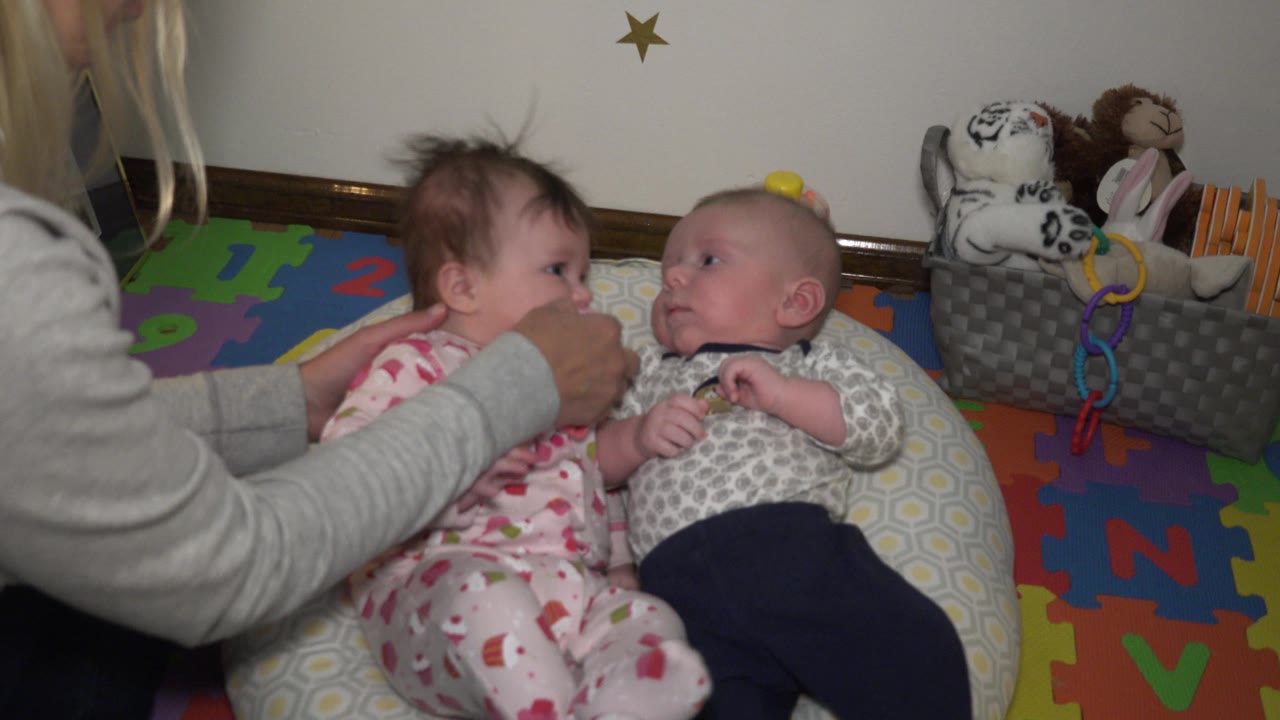 Two babies face each other as an adult hand rests between them.