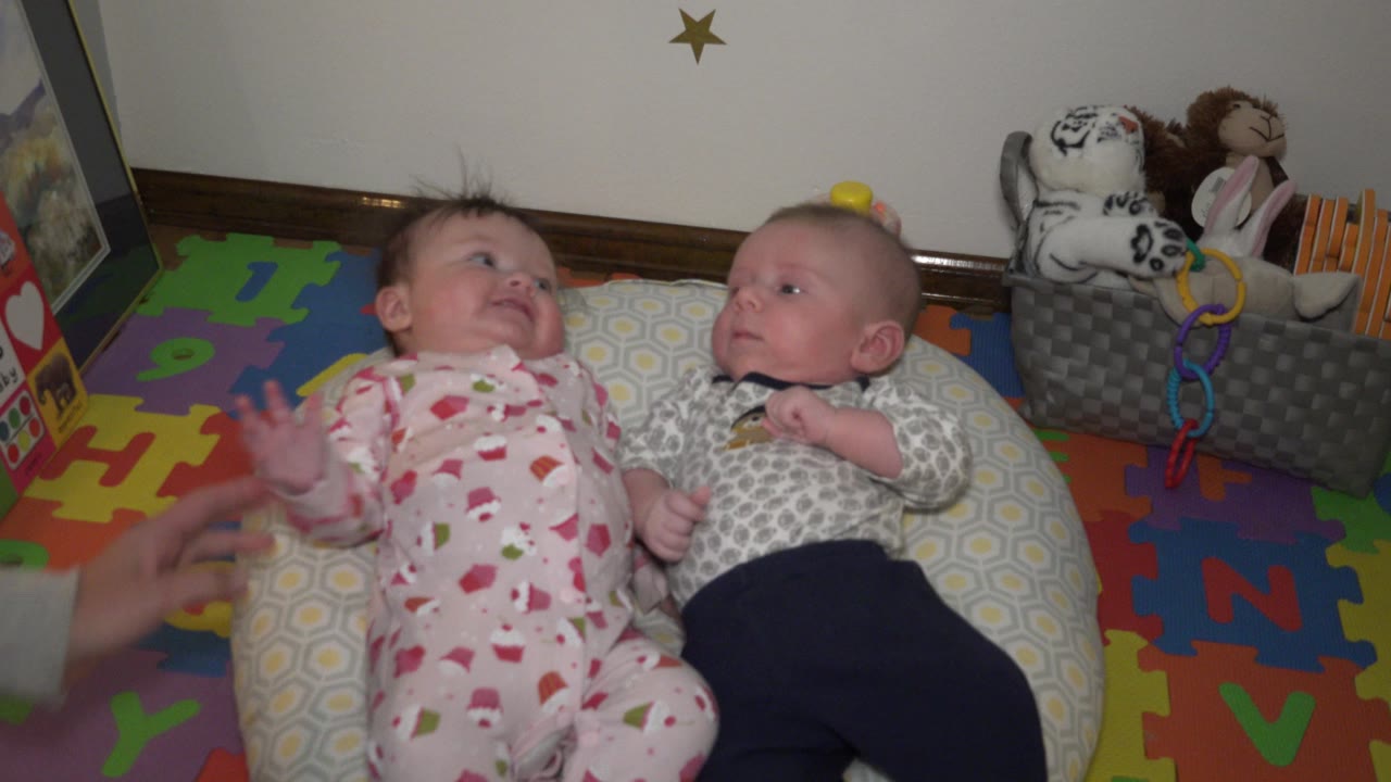 Two babies looking toward each other on floor pillows.