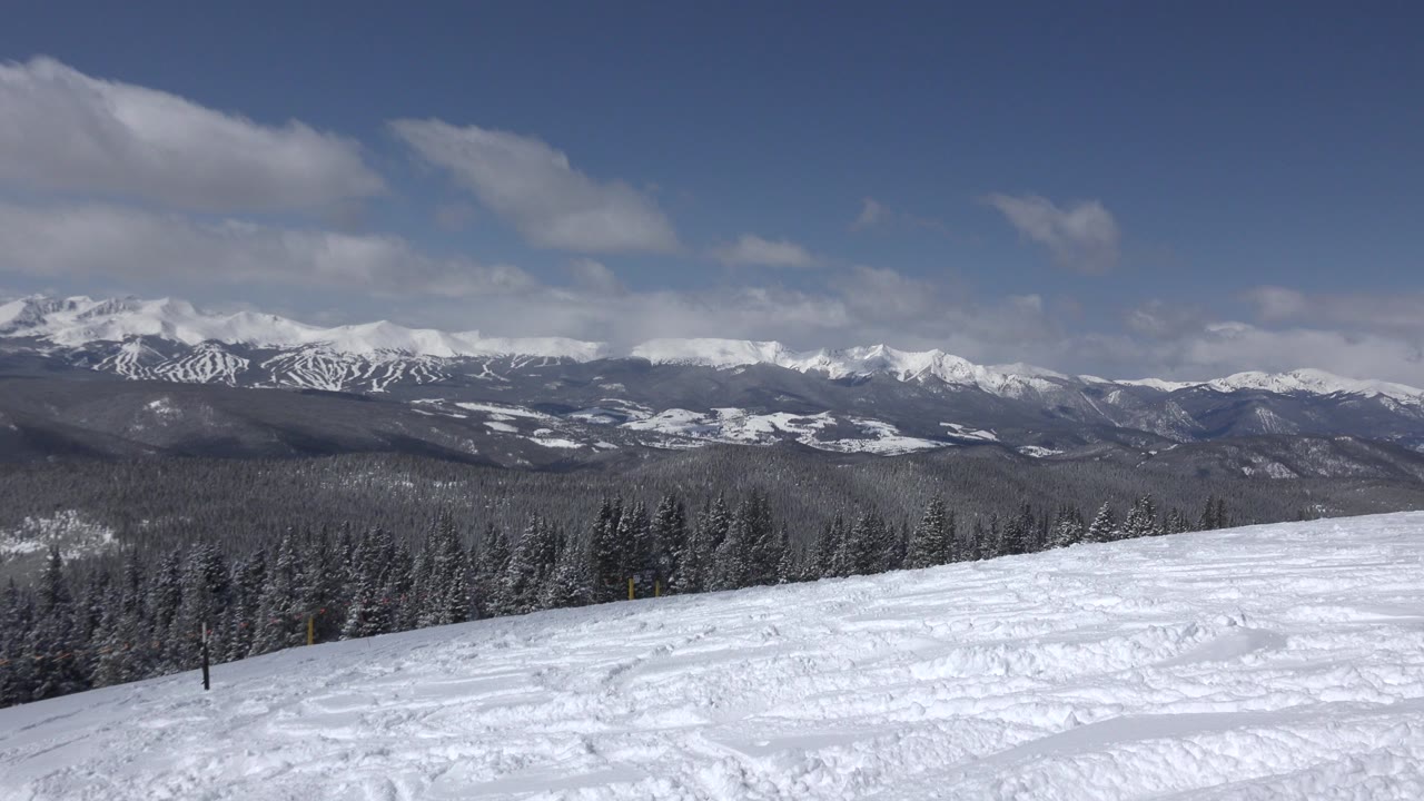 Snowy slope with evergreen forest and distant mountain range.